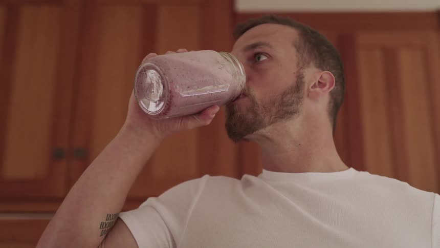 Man stands in kitchen drinking smoothie from glass jar