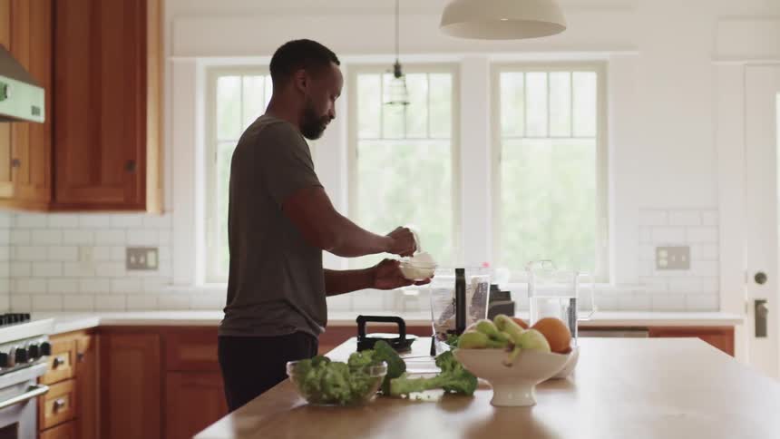 A man places food items into a blender in a home kitchen