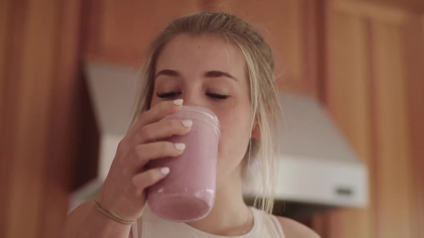 Blonde woman drinks a smoothie made from fruit and yogurt or ice cream mixed together