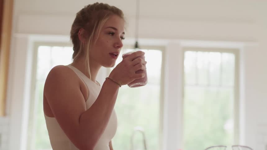 Woman wearing a white tank top takes a drink from a cup