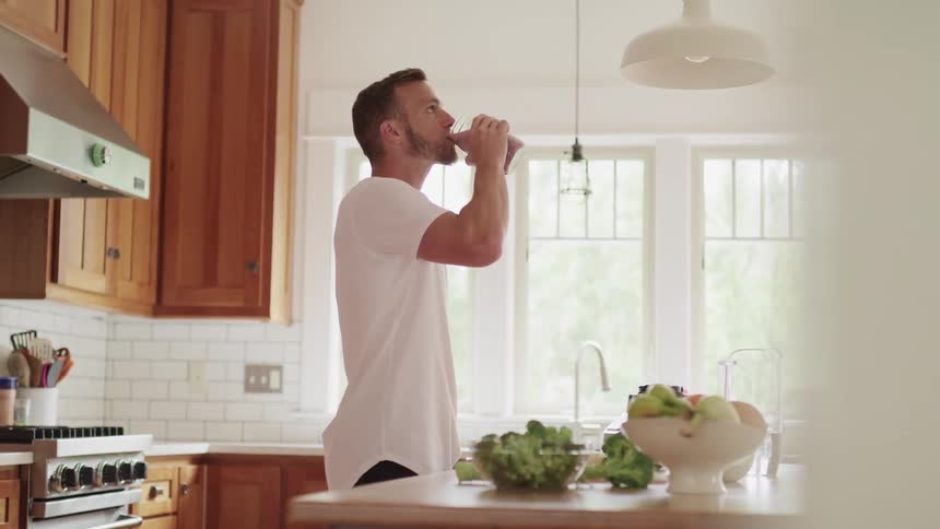 Man with a white t shirt drinks a smoothie in the kitchen at home