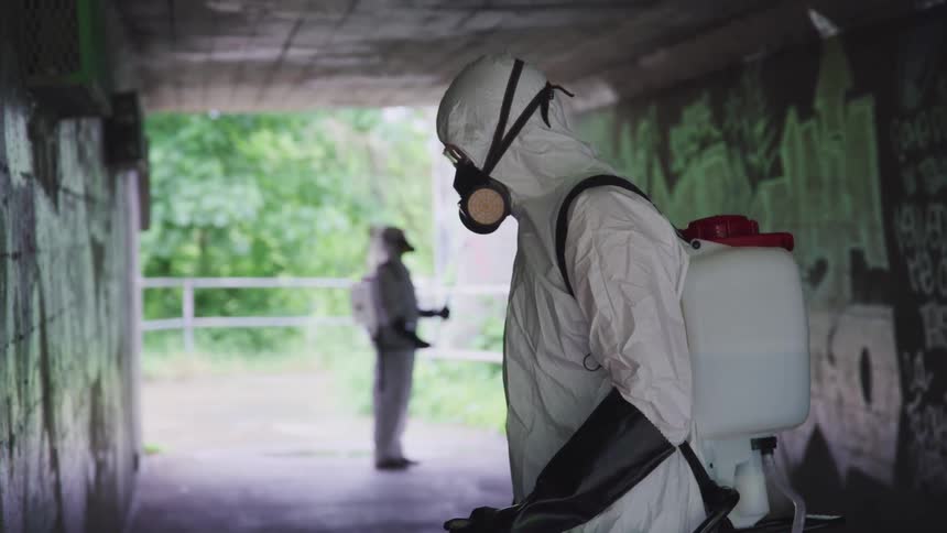 Two men spraying chemicals on the walls of a tunnel