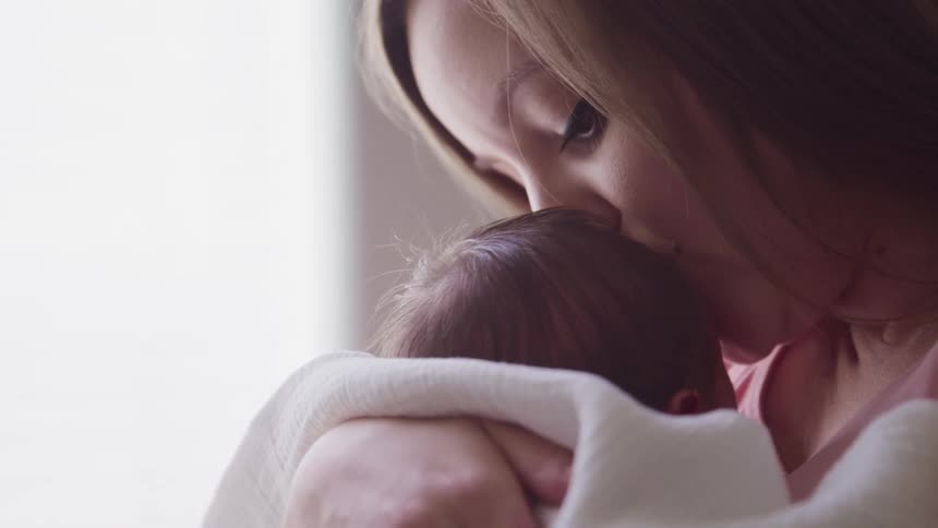Mother with a diamond nose ring holds baby and kisses his forehead