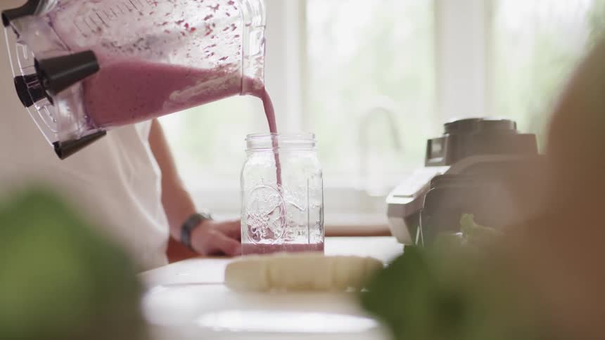 Pink beverage is poured from a blender container into a jar