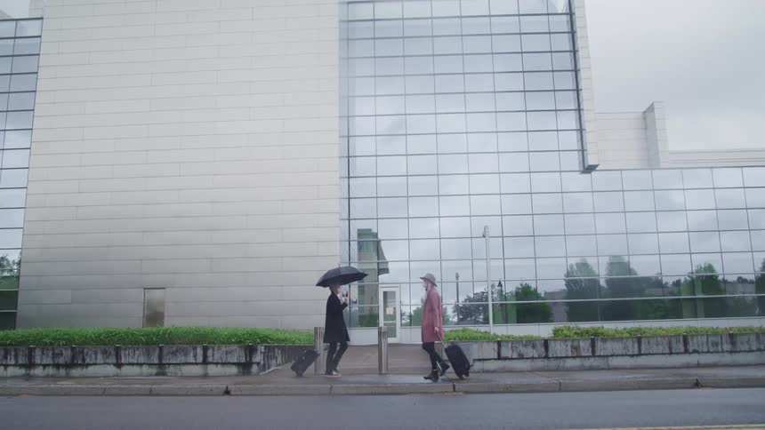 People wearing face mask and carrying luggage cross each other while walking on the sidewalk