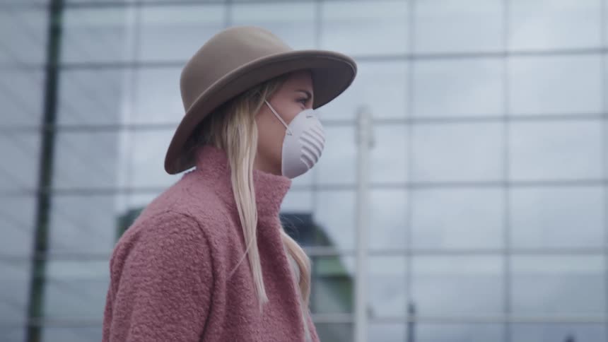 A woman wears a face mask as she walks past a reflective skyscraper