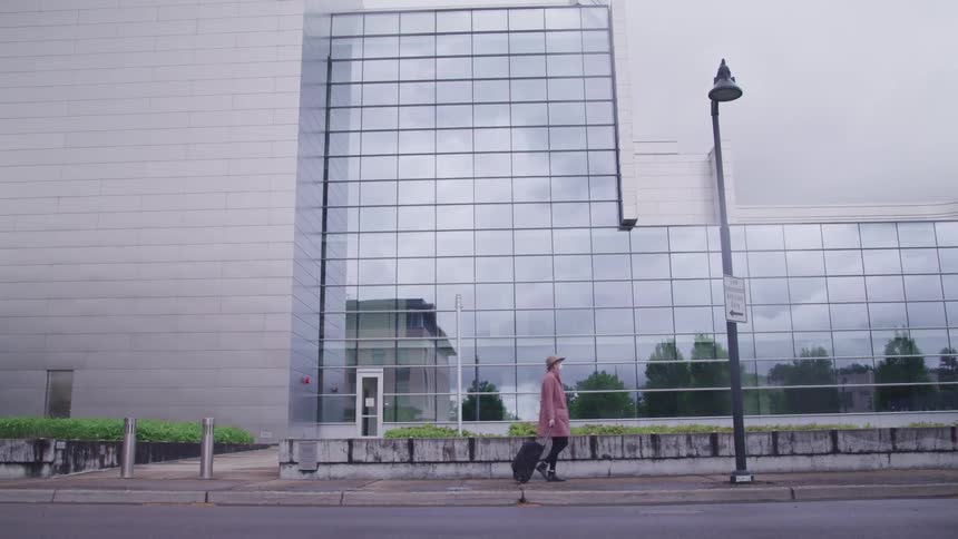 Woman walks past a building pulling luggage behind her