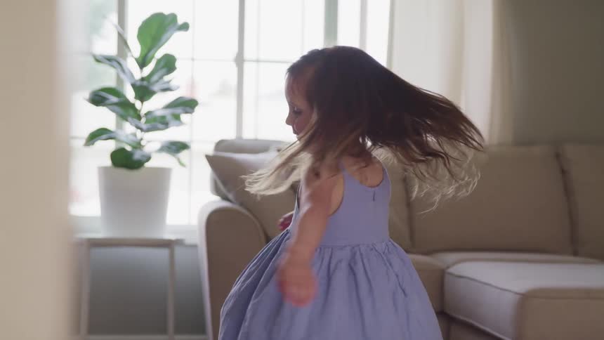 Female child twirls around in a circle in the living room as her dress swirls while she moves