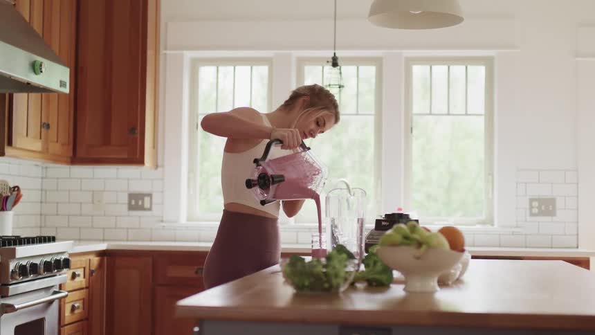 A woman pours a smoothie from a blender into a glass in a home kitchen