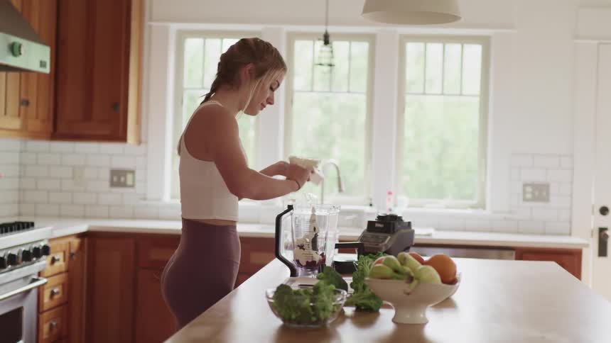 Blonde woman with tights makes a smoothie in the kitchen at home