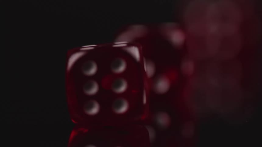 Red transparent dice with white dots rolling over a reflective surface against a black background