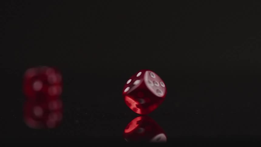 Red die with white spots spins on a corner on reflective grey surface