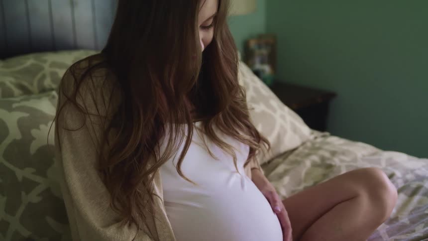 A woman rubs her pregnant belly as she looks down at it