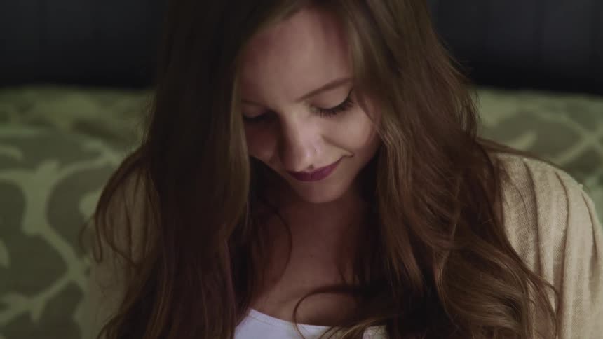 Pregnant woman with long brown hair looks down and smiles slightly