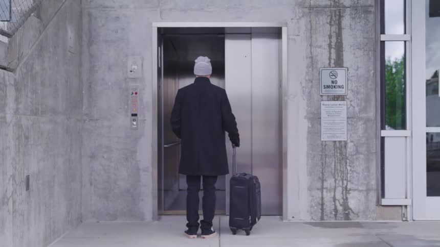 A man presses the call button on an elevator before pulling his luggage along with him into the elevator when the door opens