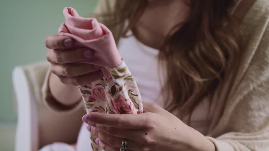 Pregnant woman with long brown hair sits in a white armchair and folds baby clothes