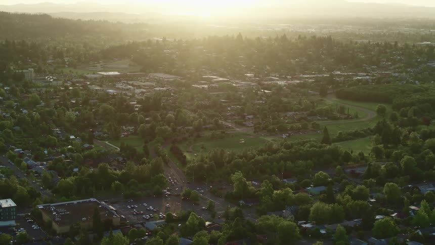 Aerial shot of a suburb at dawn showing green spaces as well as buildings and cars