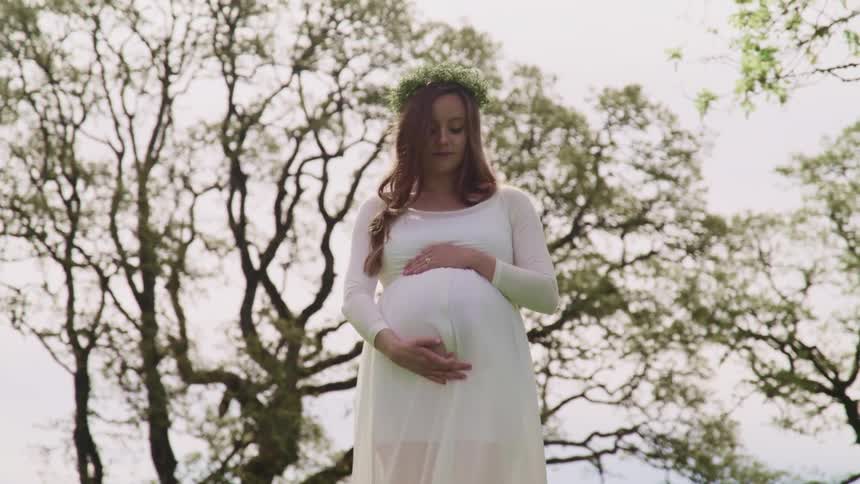 A pregnant woman in a white gown rubs her belly