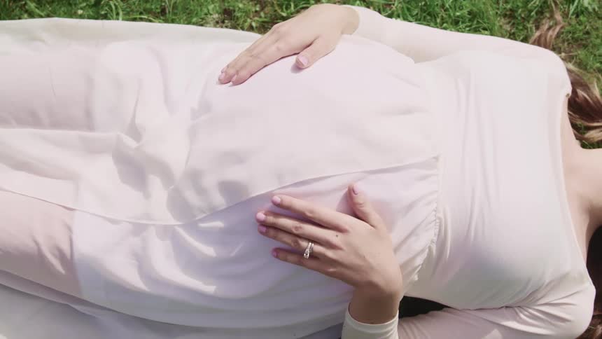 Pregnant woman lying on back on grass strokes her abdomen