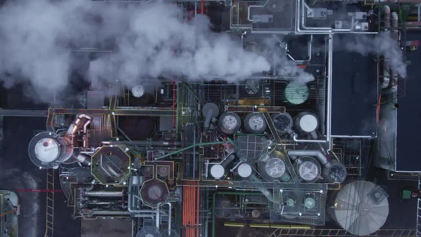 Smoke billowing from the smokestacks of a refinery during the day