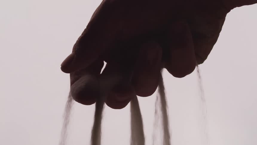 Sand slowly falls from between the fingers of a clenched hand