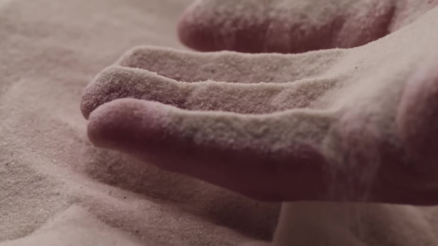 Close up of a hand lifting fine sand and then letting it flows through its fingers