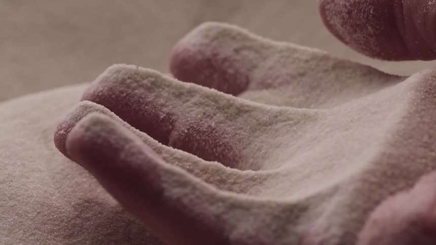 A person lifts their open hand from a pile of fine sand allowing the sand to slip through their fingers