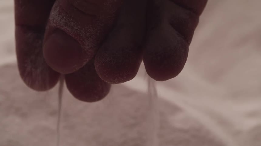 A person holding sand between their fingers allows it to fall back to the ground
