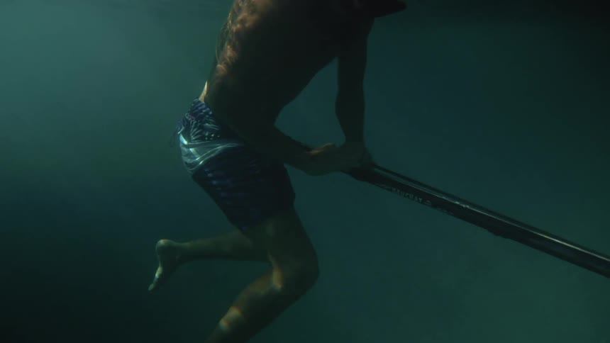 A young man under water with a big pole