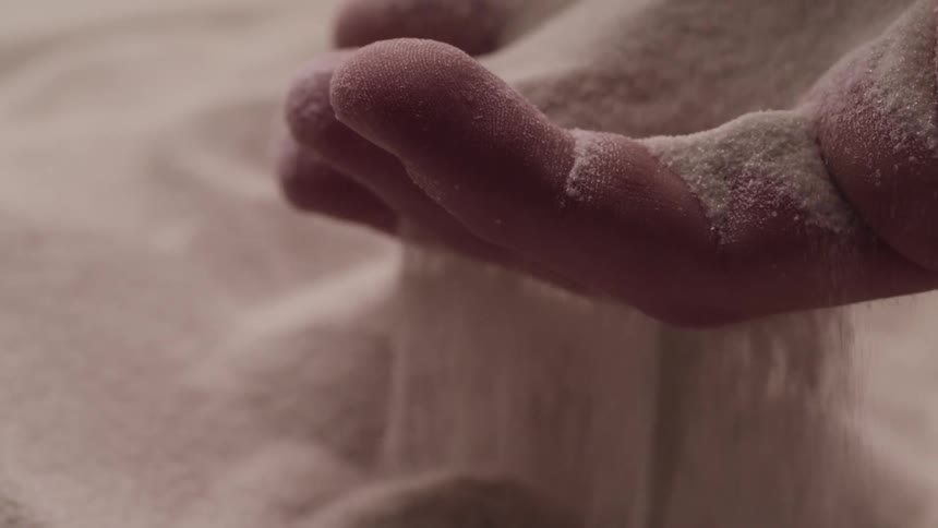 Close up of fine grains of sand filter through the fingers of a hand