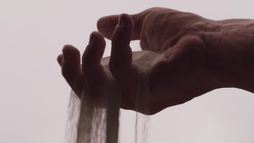 A man with a handful of sand opens his hand as the sand falls through his fingers