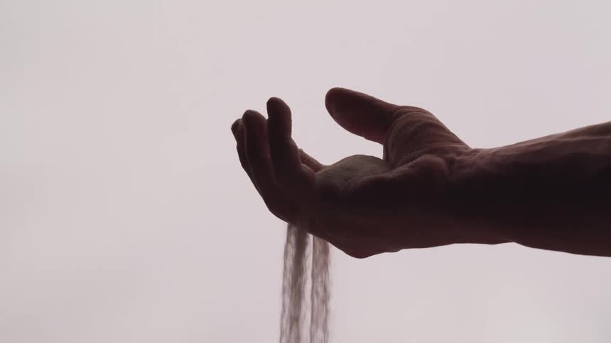 Male hand lifting sand and letting it filter through its fingers