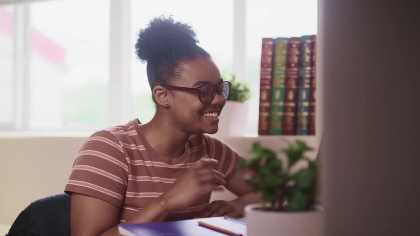 Young woman waves and smiles talking to someone else in a video call on a laptop