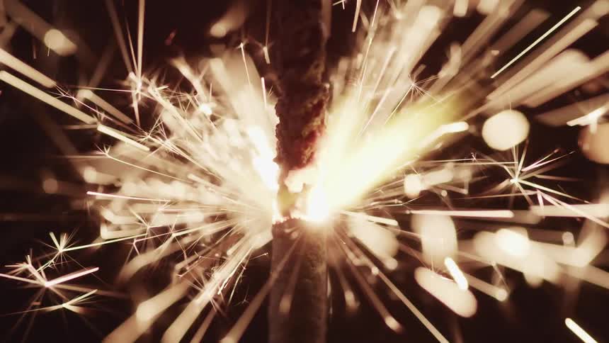 Sparks fly off of a fireworks sparkler at night