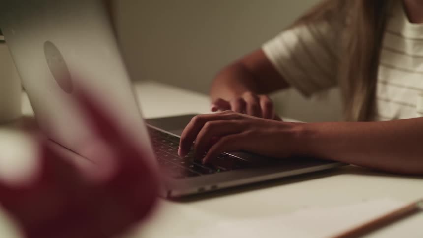 A young girl sits at her desk and types on a laptop