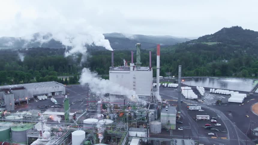 Power plant or factory spews white smoke near a lake close to the mountains