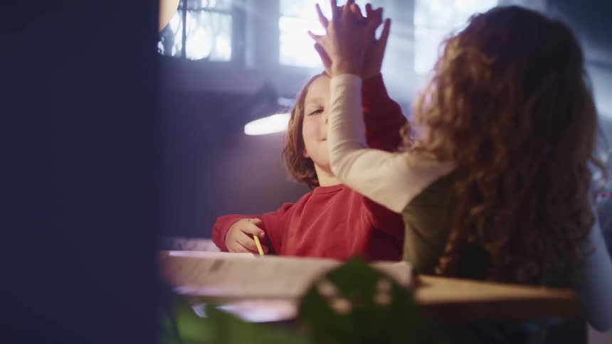 Two young children sitting at a table high five each other