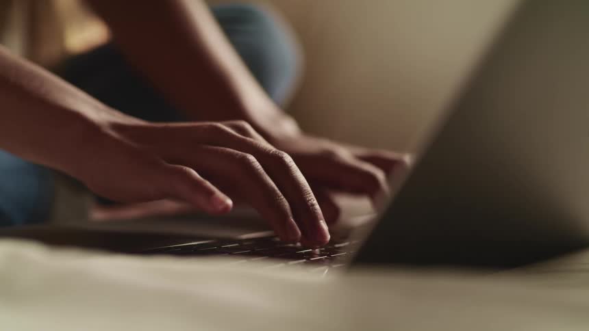 A female sitting cross legged types on the keyboard of a laptop