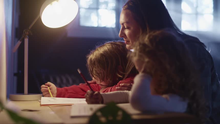 A woman sits at a desk with her young children doing school work