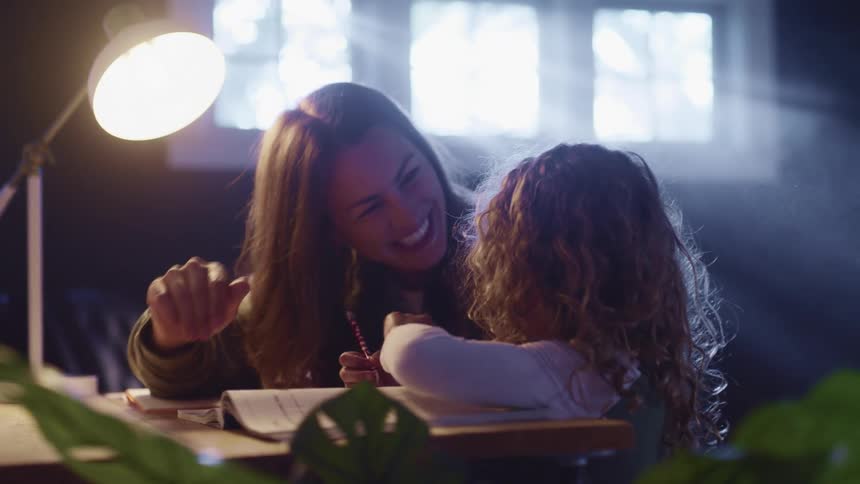 A mother high fives her daughter and smiles as she does school work