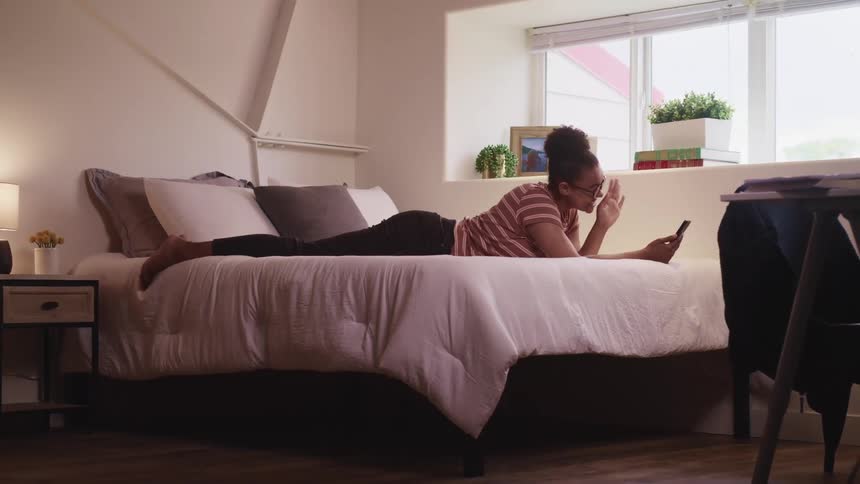 Young woman lays in bed while talking on her smartphone