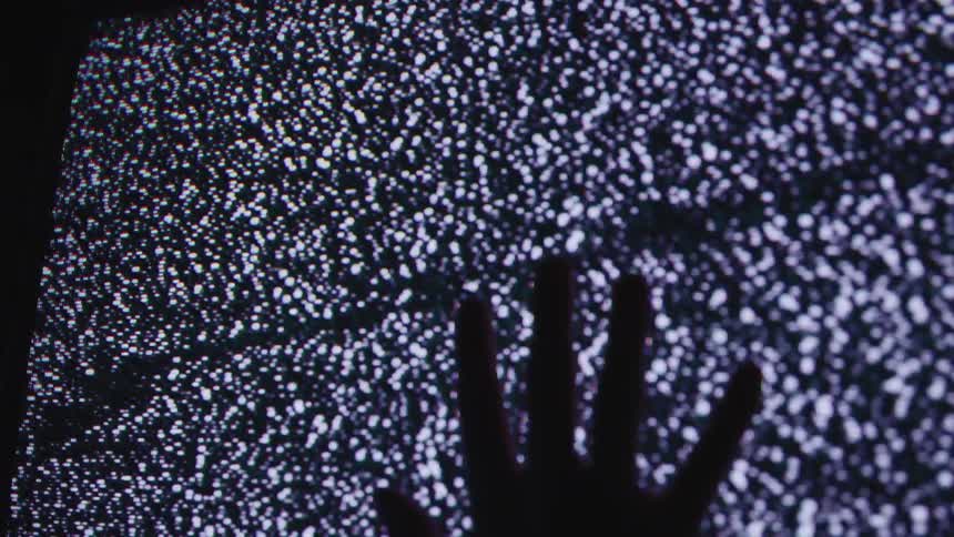A hand is held up against an old tv with static in the dark