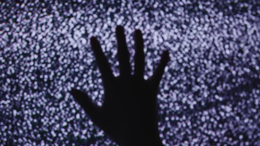 Hand silhouetted by snowy signal noise of console