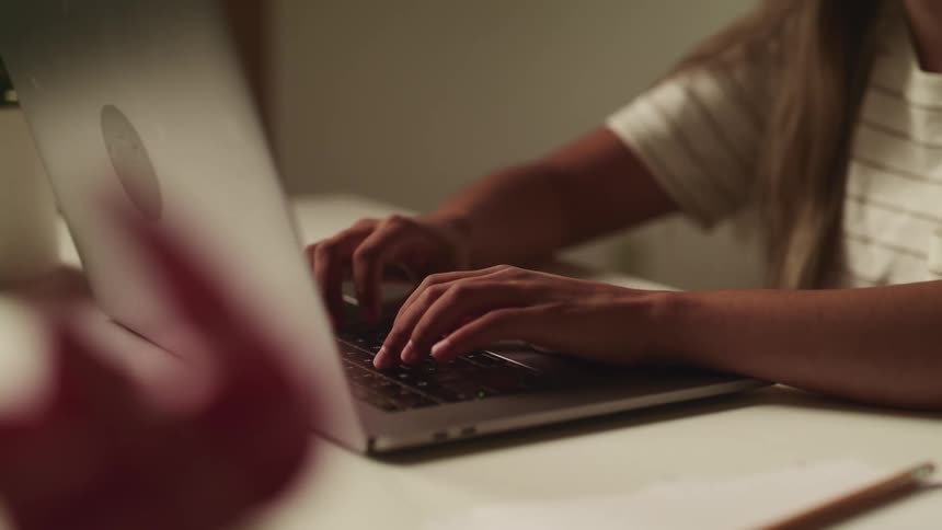 A young girl types on her laptop at her desk