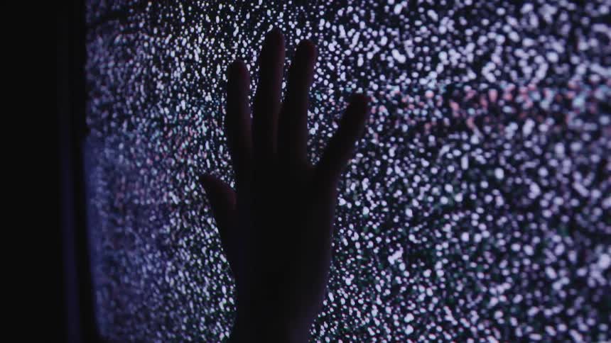A hand touches a static filled television in a dark room