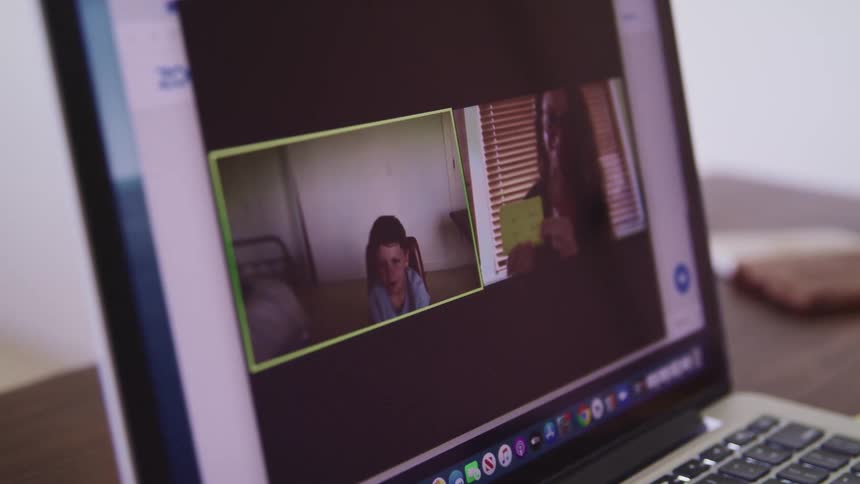 A teacher provides a lesson using flash cards with a small child watching her via teleconferencing software