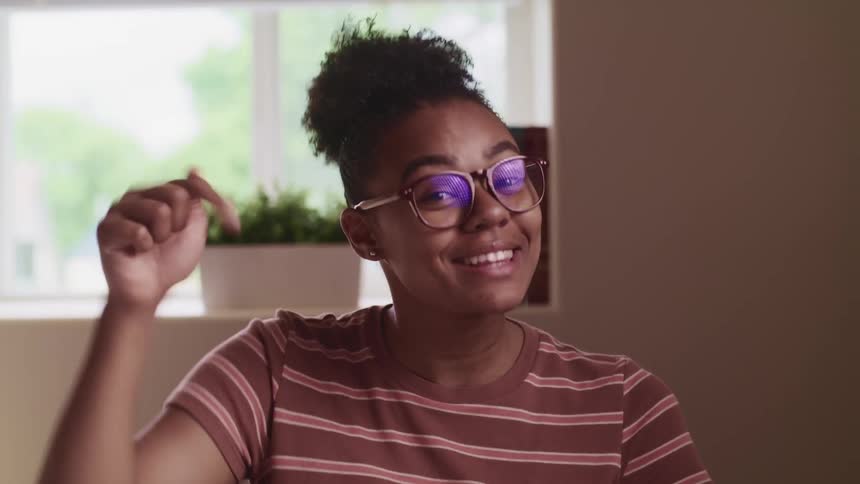 Black woman with glasses and striped t shirt sitting at a desk laughs and talks to the camera