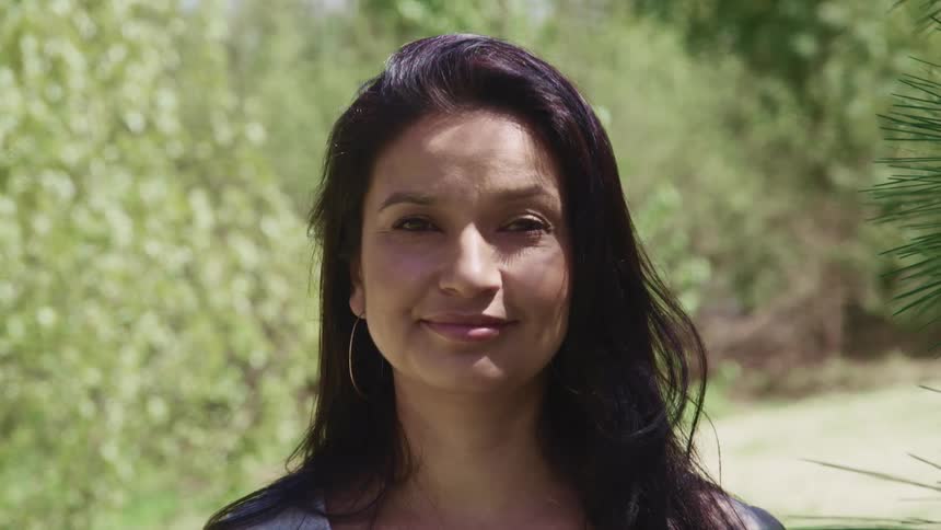 Brunette woman with straight dark hair and earrings smiles slightly and stares at the camera