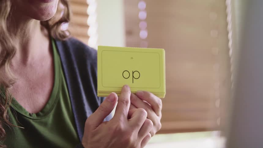 A woman with long curly hair holds a flash card with two letters printed on it