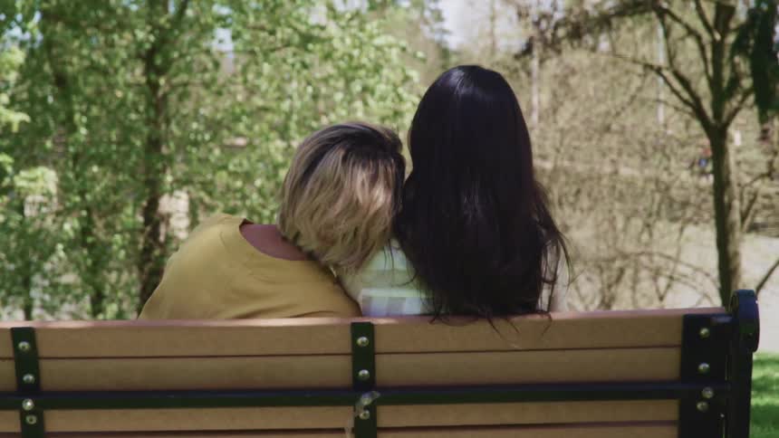 Couple sit on park bench with one leaning head on the others shoulders